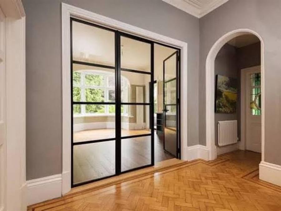Black steel-look internal aluminium double doors and glazed side door between a period hallway and a bay-windowed reception room, with parquet flooring